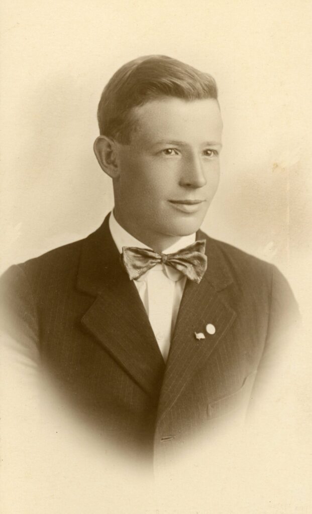 Head and shoulder photo of a teen boy wearing a bow tie, white shirt and jacket with two lapel pins.