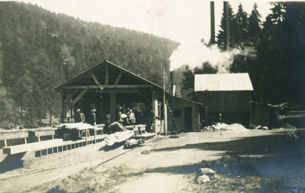 Mill building with pile of sawdust on the right in front of the smaller shed. 