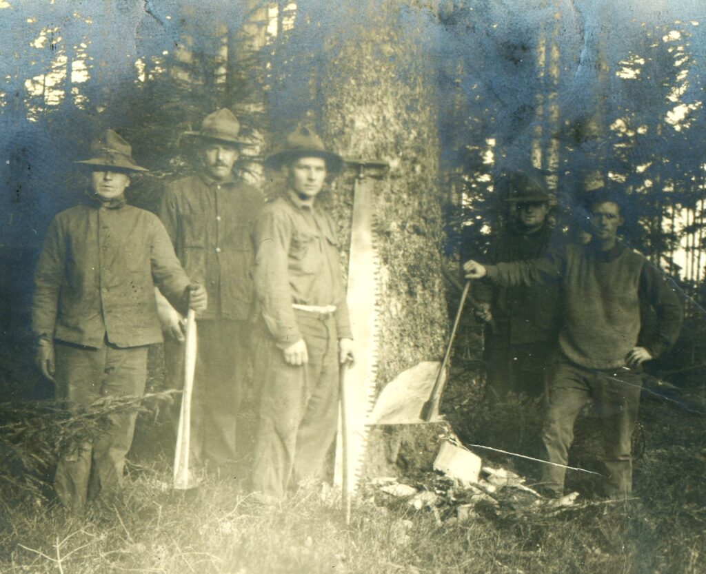 five men pose in front of a tree with axes and a crosscut saw