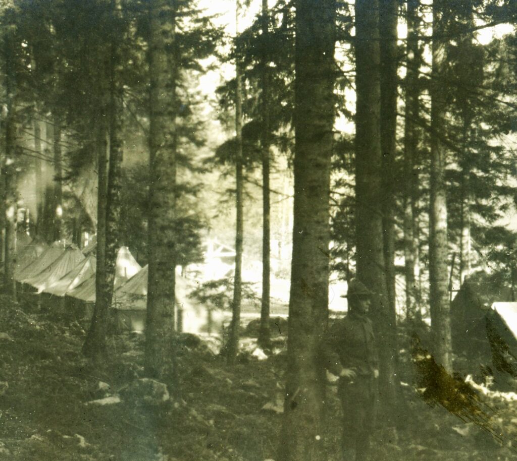 A soldier stands with tents in the background. 