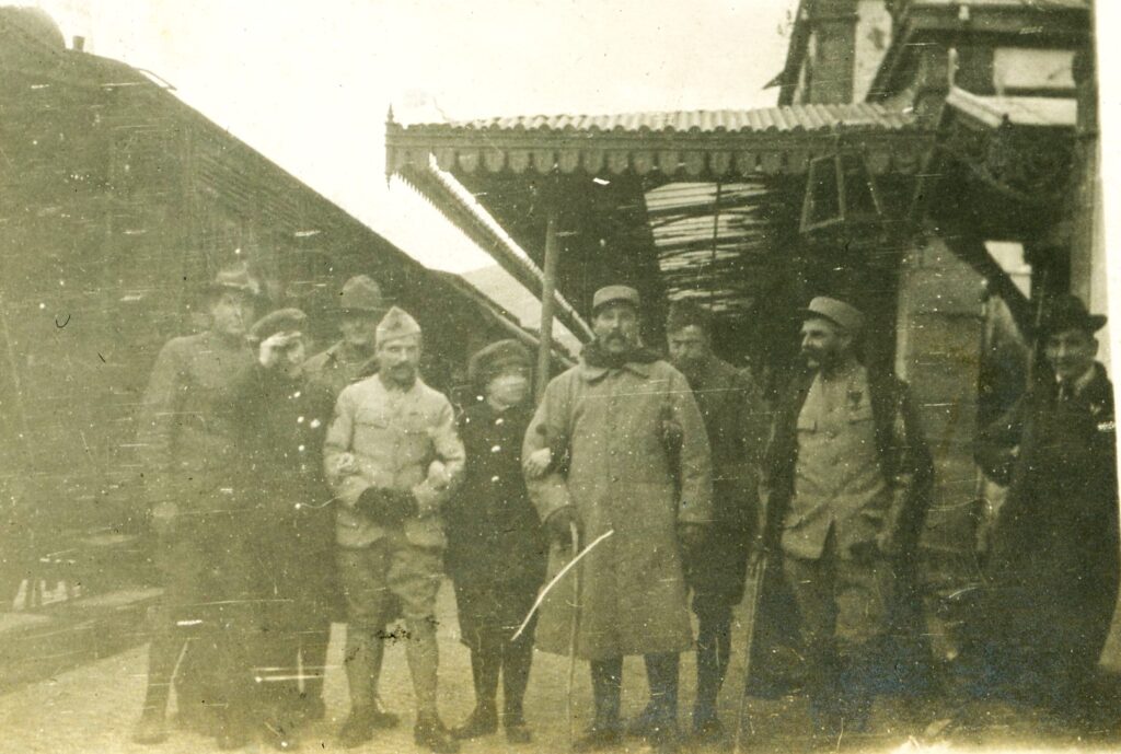 a group of soldiers and civilians stand under an awning along a French street.